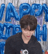 a young man is standing in front of a wall with blue balloons .