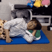 a man is laying on a blue mat with a stuffed animal pillow .