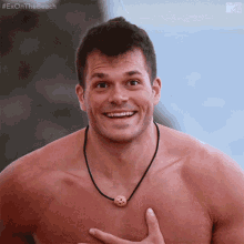 a shirtless man wearing a necklace with a cookie on it is smiling for the camera