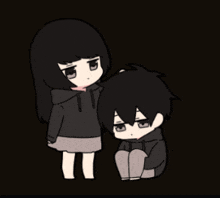 a girl stands next to a boy who is sitting down