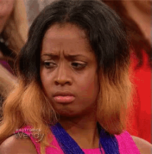 a woman wearing a pink top and a blue necklace is making a funny face .
