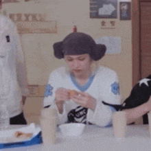 a person wearing a hat and ear muffs is sitting at a table with a bowl of food .