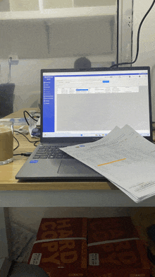 a stack of hard copy paper sits next to a laptop on a desk