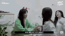 a group of women are holding hands in a room . one of the women is wearing devil horns .