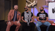 three men are sitting on a couch and one has a shirt that says athletes rule
