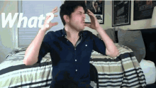a man in a blue shirt is sitting on a bed with his hands on his head and the words what written above him
