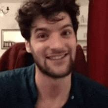 a man with a beard is smiling and looking at the camera while wearing a blue shirt .
