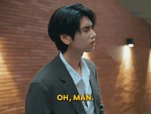 a man in a suit and white shirt is standing in front of a brick wall and says oh man .