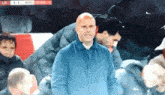 a man in a blue jacket stands in front of a scoreboard that says liv 5-1 whu 93.49 + 5