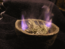 a bowl of burning sage leaves on a black blanket