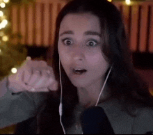 a woman wearing headphones is making a funny face while sitting in front of a christmas tree .