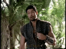 a man with a beard is standing in the middle of a forest .