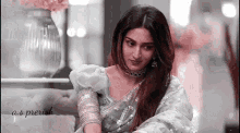 a woman in a gray saree is sitting on a couch .