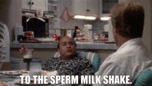 two men are sitting at a table talking to each other and one of them is saying `` to the sperm milk shake ''