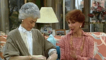 two older women are sitting on a couch in a living room .