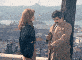 a man and a woman are standing next to each other on a balcony overlooking a city