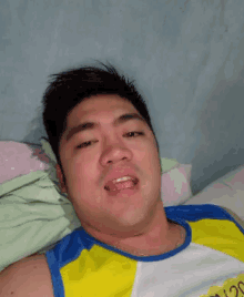 a man wearing a blue and yellow tank top is laying on a bed