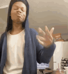 a woman wearing a blue hoodie and a white shirt is making a funny face while standing in a kitchen .