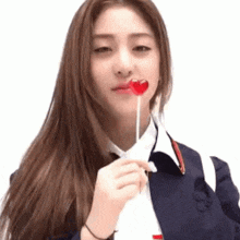 a girl in a school uniform is holding a heart shaped lollipop in her mouth .