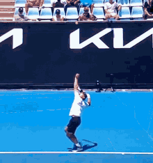a man is serving a tennis ball on a blue court in front of a wall that says kv