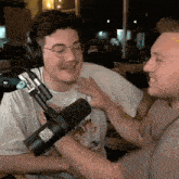 a man wearing glasses and headphones is talking to another man in front of a microphone with a qr code on it