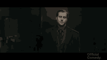a man in a suit and tie is standing in a dark room with the words official comedy on the bottom right