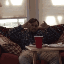 a man in a plaid shirt is sitting on a couch giving the thumbs down sign