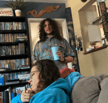 a man with long hair stands behind a woman sitting on a couch holding a cup