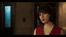 a woman in a red dress and hat is standing in a hallway .