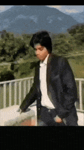 a man in a suit and white shirt stands on a balcony with mountains in the background