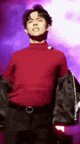 a man in a red turtleneck and black pants is standing on a stage