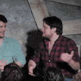two men in plaid shirts are talking to each other in front of a crowd