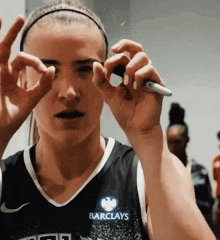 a woman wearing a barclays jersey holds a marker