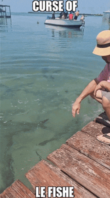 a man sitting on a dock holding a fish with the caption curse of le fishe below him