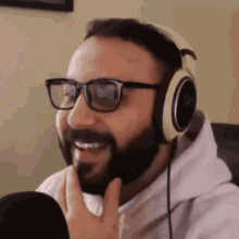 a man with a beard wearing headphones and glasses is smiling .
