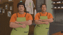 two men wearing green aprons are standing next to each other in a restaurant
