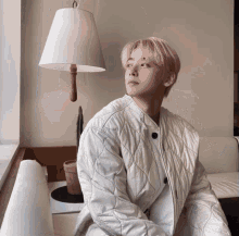 a man with pink hair is sitting in front of a white lamp