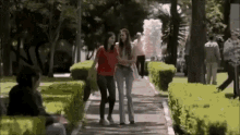 two women are walking down a sidewalk in a park