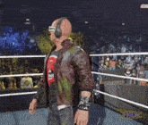 a bald man wearing headphones stands in a wrestling ring with a snickers logo behind him