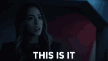 a woman in a black jacket stands in front of a sign that says " this is it "
