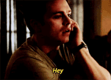 a man is talking on a cell phone and the word hey is on his shirt