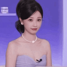 a woman wearing a pearl necklace and a strapless dress is smiling