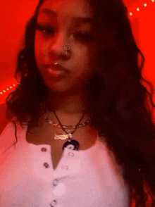 a woman wearing a necklace and a nose ring is standing in front of a red background .