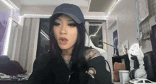 a woman wearing a blue hat and a black hoodie is sitting in a room