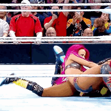 a woman with pink hair is laying on the floor in a wrestling ring .