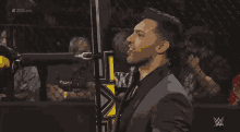 a man in a suit stands in front of a wrestling ring with the words # 205live in the corner