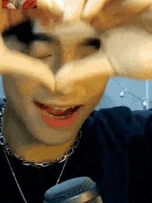 a close up of a person making a heart with their hands in front of a microphone