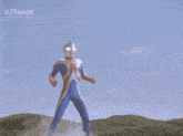 a cartoon character from ultraman is standing in a field with a blue sky in the background .