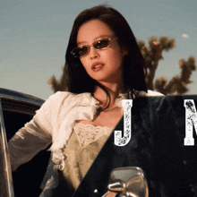 a woman wearing sunglasses is standing next to a car with the letter j in the corner