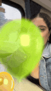 a woman blowing a green bubble with a yellow balloon in the background